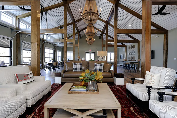 Inviting open-concept clubroom area featuring rustic wood beams, elegant chandeliers, and plush seating for a cozy ambiance.