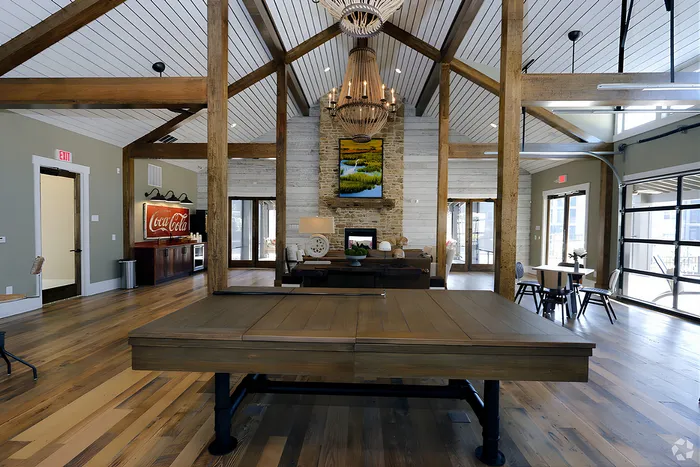 Luxurious open-concept clubroom space featuring rustic wooden beams, elegant chandelier, and a cozy seating area with a fireplace.