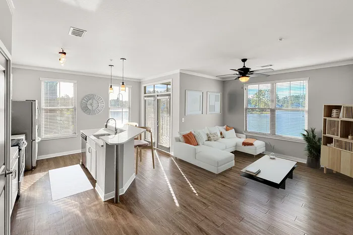 Bright and modern open-concept living room with a cozy white sectional sofa, elegant kitchen island, and large windows offering stunning water views.