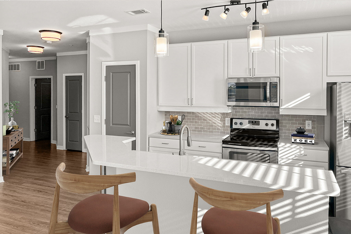 Modern kitchen with sleek white cabinetry, stainless steel appliances, and elegant lighting, complemented by a stylish breakfast bar with wooden chairs.