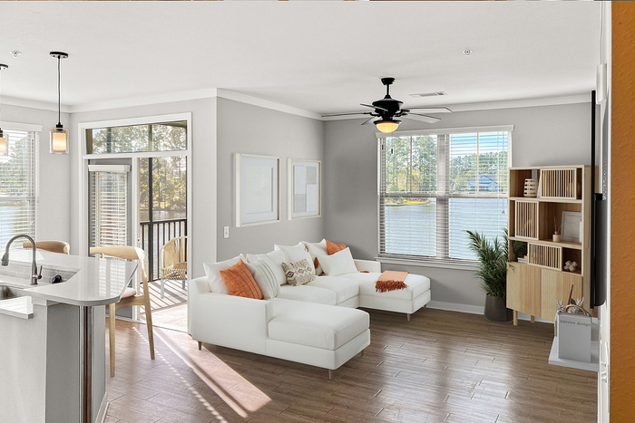 Bright, modern living room with large windows showcasing stunning lake view, complemented by elegant white and orange decor.