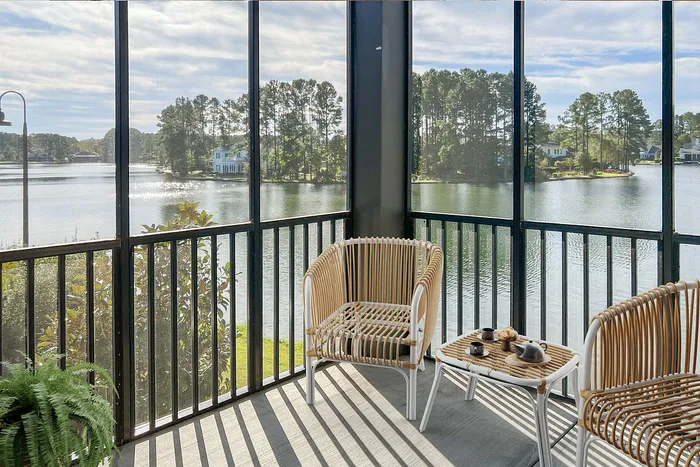 Charming screened-in porch with lake view, featuring cozy wicker seating and coffee set, perfect for relaxation.