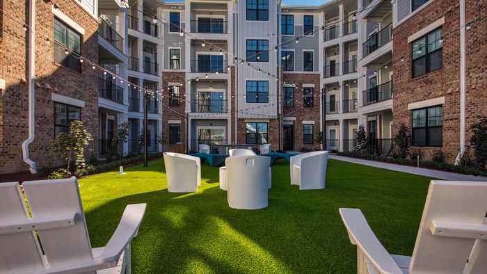 Charming apartment courtyard featuring modern white seating, lush green lawn, and string lights, perfect for relaxation and gatherings.