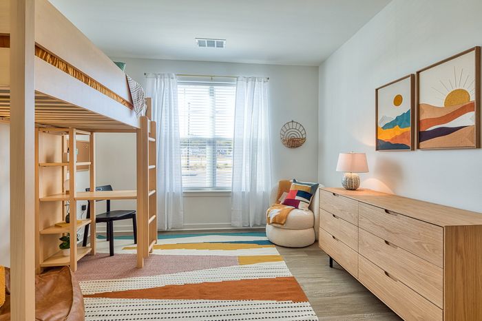Bright and cozy bedroom with a stylish loft bed above a functional study area, complemented by colorful art and a large window with natural light.