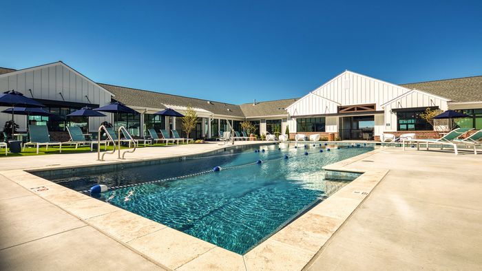 Luxurious outdoor swimming pool surrounded by modern lounge chairs and stylish buildings under a clear blue sky.