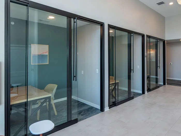 Modern office corridor featuring sleek glass-walled meeting rooms and stylish overhead lighting.