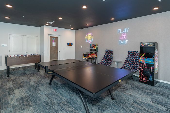 Vibrant game room featuring a ping pong table, foosball, and vintage arcade machines with playful neon signs.