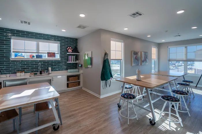 Bright and airy creative studio with modern wooden tables, colorful stools, and a sleek kitchenette, perfect for artistic inspiration.