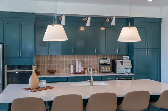 Modern kitchen featuring elegant blue cabinetry, a stylish marble island with seating, and chic lighting fixtures.
