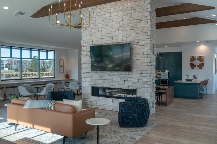Modern living space with a cozy leather sofa, stone fireplace with TV, and a vibrant kitchen featuring teal cabinetry and bar seating, enhanced by natural light and elegant decor.