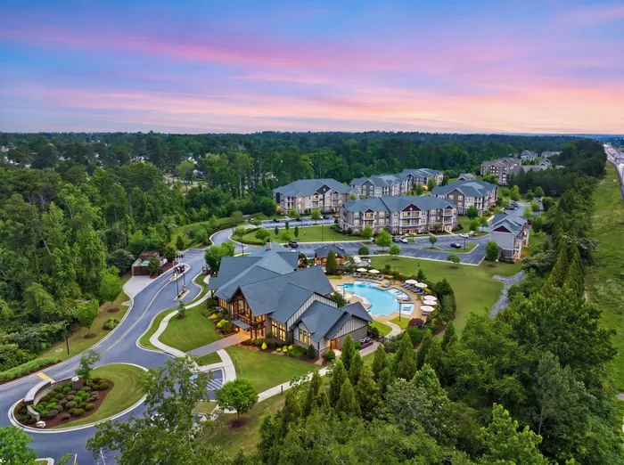 Stunning aerial view of a luxurious residential complex nestled amidst lush greenery, featuring stylish multi-story buildings and a pristine pool area at sunset.
