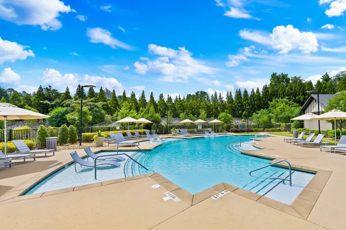 Luxurious outdoor pool area with stylish lounge chairs, surrounded by lush greenery and bright blue skies.