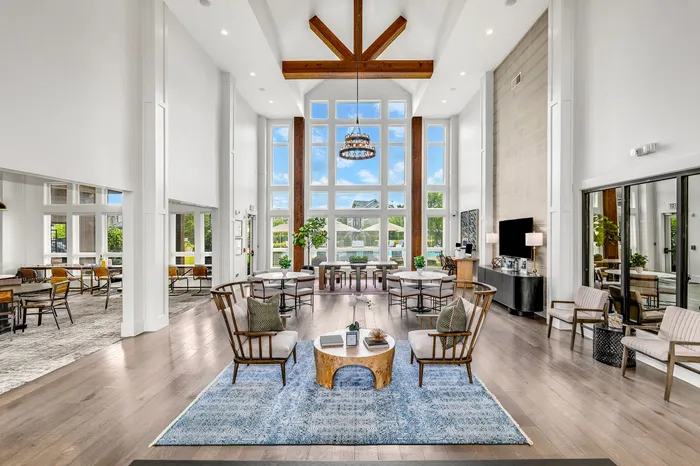Luxurious living area featuring a high ceiling with exposed beams, large windows offering abundant natural light, stylish seating arrangements, and contemporary decor.