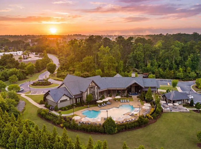 Stunning aerial view of a luxurious estate with a modern design, featuring a sparkling pool and lush greenery set against a breathtaking sunset.