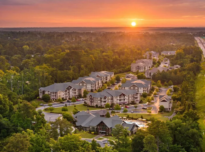 Gorgeous aerial view of modern apartment complex nestled in lush greenery with a captivating sunset backdrop, offering serene and upscale living.