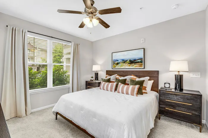 Elegant bedroom with a king-sized bed, modern ceiling fan, and large window offering a beautiful garden view.