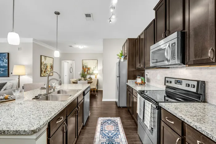 Elegant kitchen and dining area with granite countertops, dark wood cabinets, modern appliances, and stylish lighting.