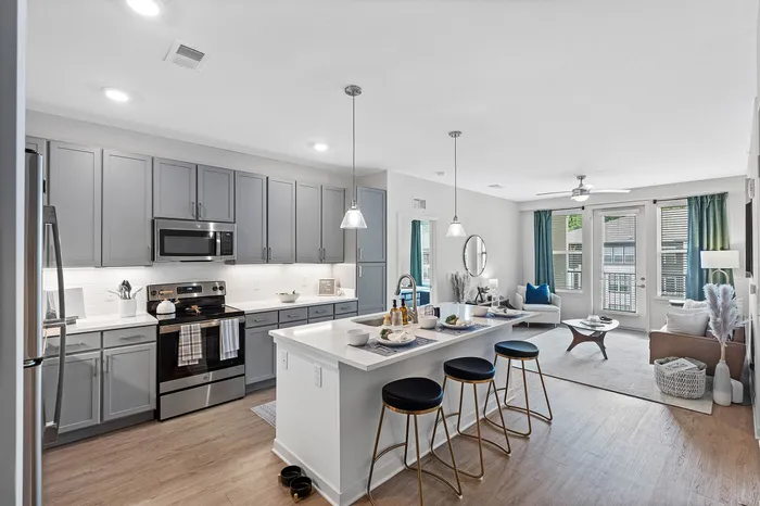 Bright and modern apartment with sleek grey kitchen cabinets, spacious breakfast bar with stylish barstools, open living area featuring large windows and trendy decor.