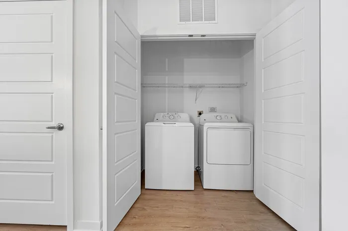 Modern laundry space with a sleek washing machine and dryer, enclosed by elegant white doors and featuring ample shelving.