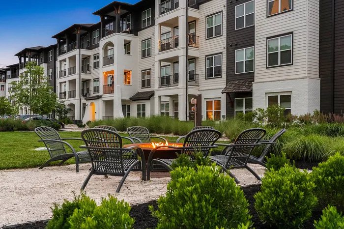 Charming apartment complex exterior with cozy fire pit seating area amidst lush greenery, perfect for relaxation.