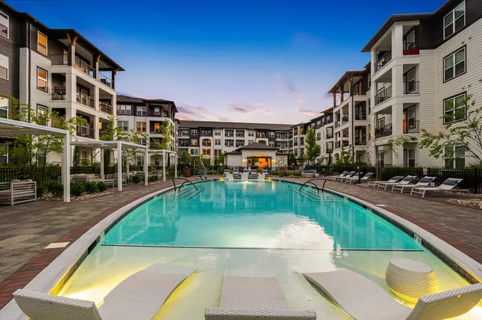 Luxurious apartment complex with a sparkling outdoor pool, surrounded by modern multi-story buildings and elegantly landscaped gardens.