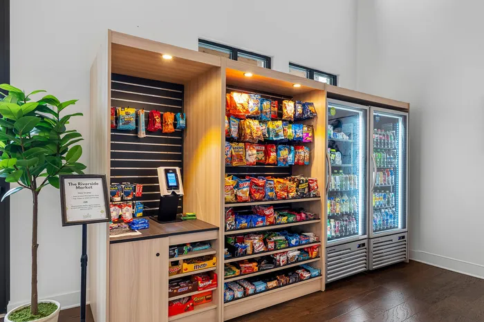 Chic and convenient apartment amenity featuring a brightly lit mini-market with snack shelves, cool drinks in a refrigerator, and a modernized payment kiosk.