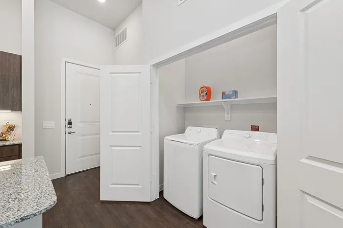 Modern apartment entryway featuring sleek hardwood floors, a spacious built-in laundry area, and elegant granite countertops.