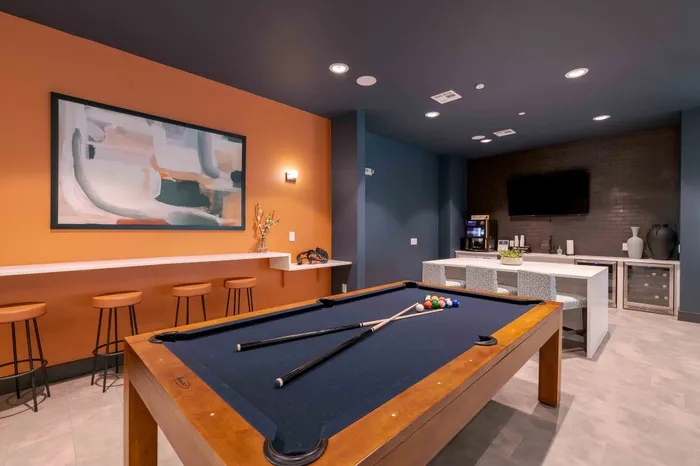Modern entertainment room with a sleek pool table, vibrant artwork, cozy bar seating, and a stylish lounge area.