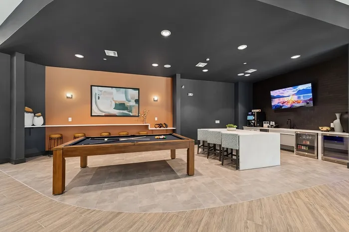 Chic game room featuring a stylish pool table, modern art, and a sleek bar area with a cozy lounge atmosphere.