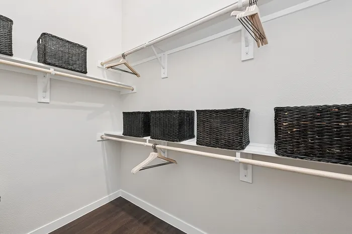 Spacious walk-in closet with elegant wooden flooring, equipped with sleek white shelves, dark woven storage baskets, and convenient hanging rods.