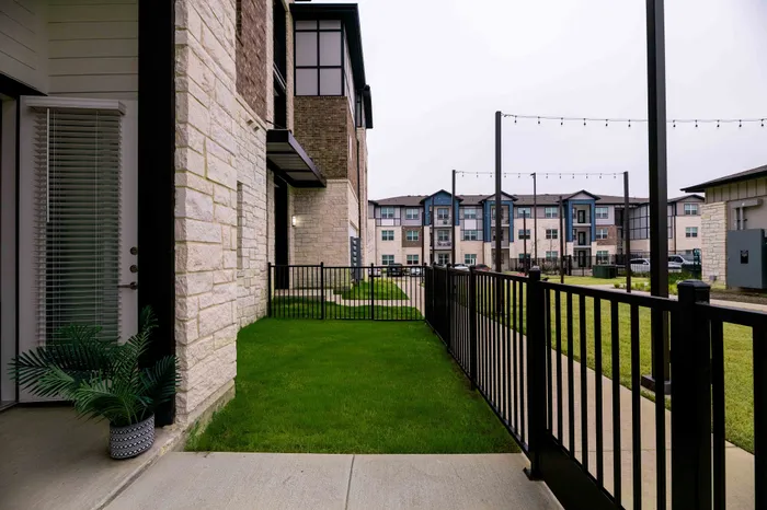 Charming apartment exterior with modern stone facade, private fenced patio, and lush green landscaping.