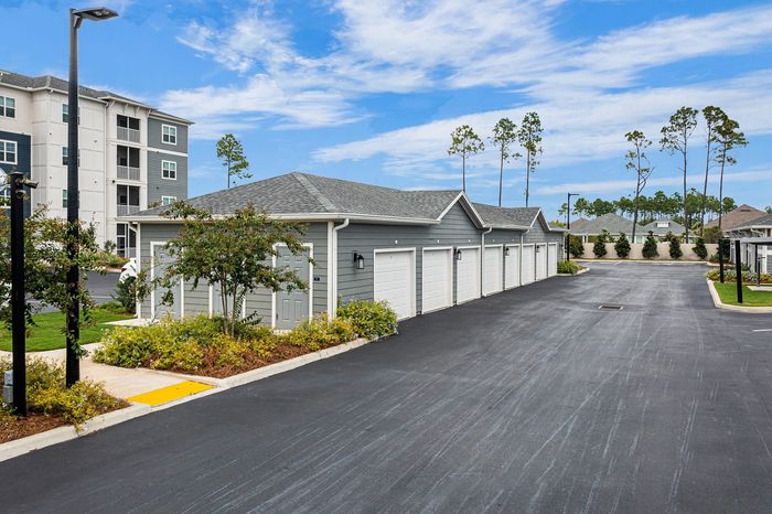 Modern apartment complex with neat exterior garages and lush landscaping, offering ample parking space and serene surroundings.
