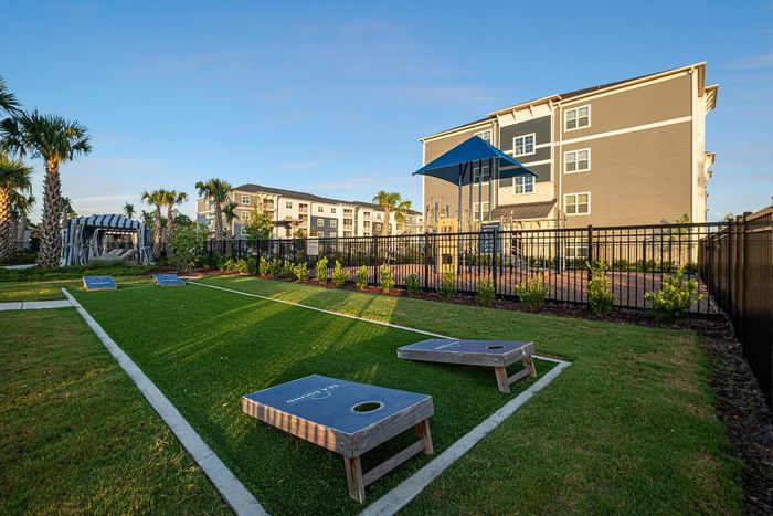 Inviting residential community with lush green landscape, cornhole game setup, and palm trees under a clear blue sky.