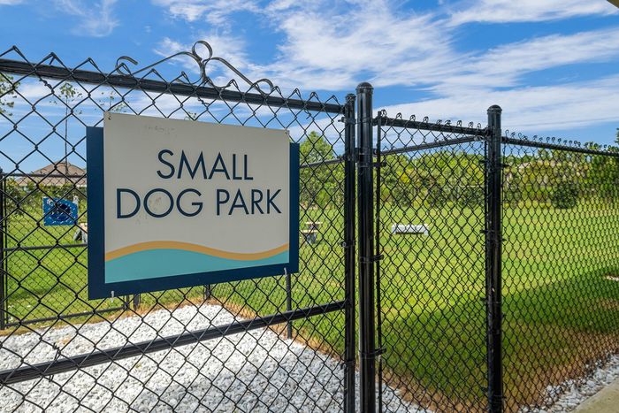 Inviting small dog park enclosed by a fence, perfect for pet-friendly living with lush green area under a clear blue sky.