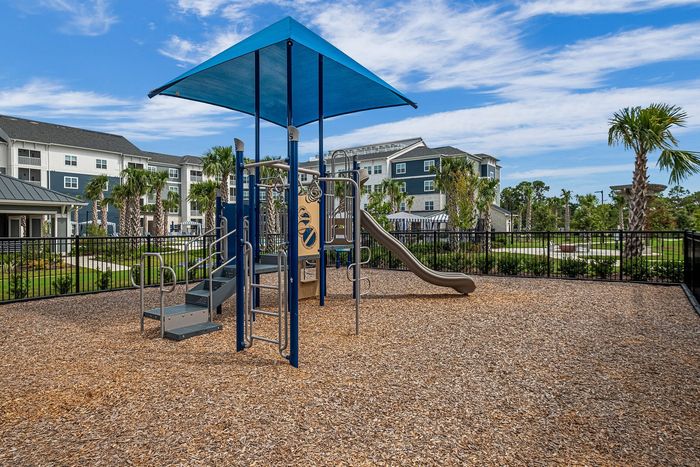 Inviting modern playground with blue canopy and slide, nestled within a serene apartment community surrounded by lush palm trees.