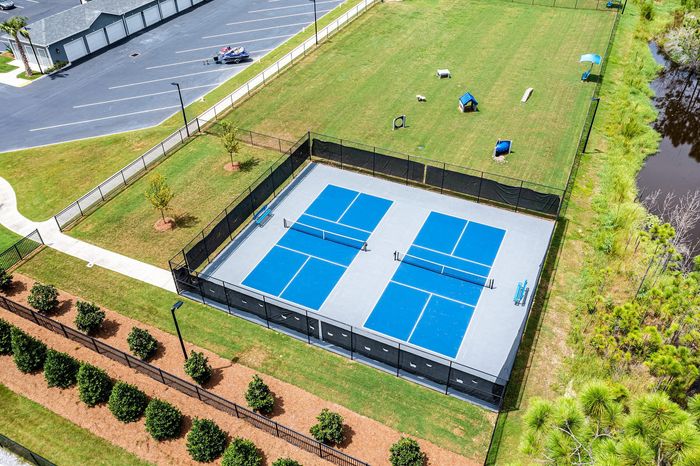 Scenic aerial view of modern blue tennis courts surrounded by lush greenery and adjacent recreational areas.