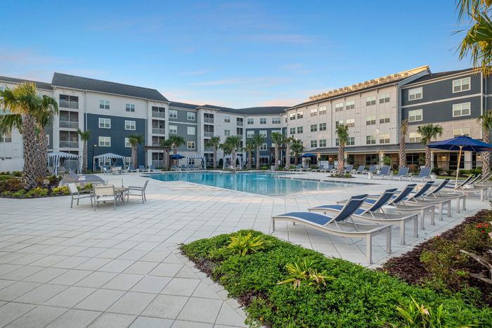 Luxurious apartment complex showcasing a stunning pool area with elegant lounge chairs and lush palm trees, perfect for relaxation and leisure.