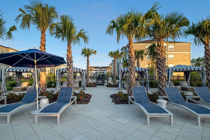 Luxurious outdoor poolside area with elegant cabanas, stylish loungers, and towering palm trees under a clear blue sky.