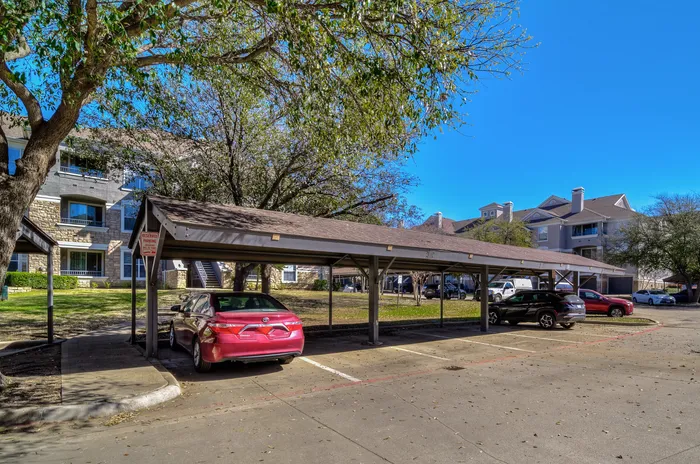 Inviting apartment complex with covered parking, lush greenery, and charming architecture under a clear blue sky.