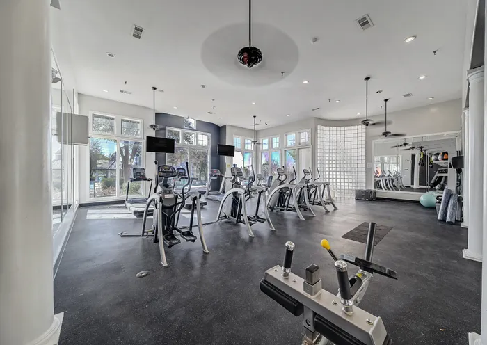 Spacious and modern gym with abundant natural light, featuring a variety of cardio equipment and exercise amenities.