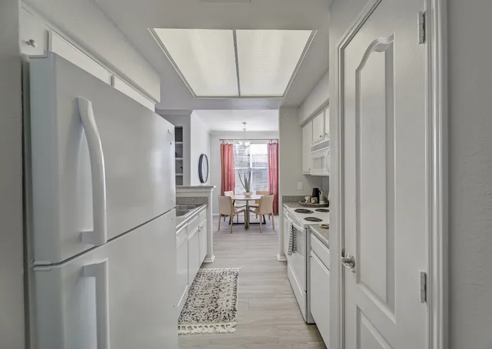Modern kitchen with sleek appliances leading to a bright dining area with elegant decor and vibrant red curtains.