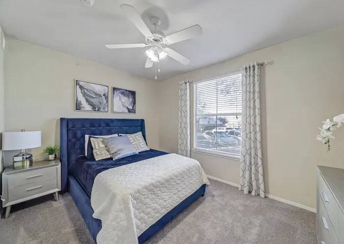 Bright and cozy bedroom with modern decor features a plush blue bed, chic artwork, and abundant natural light.