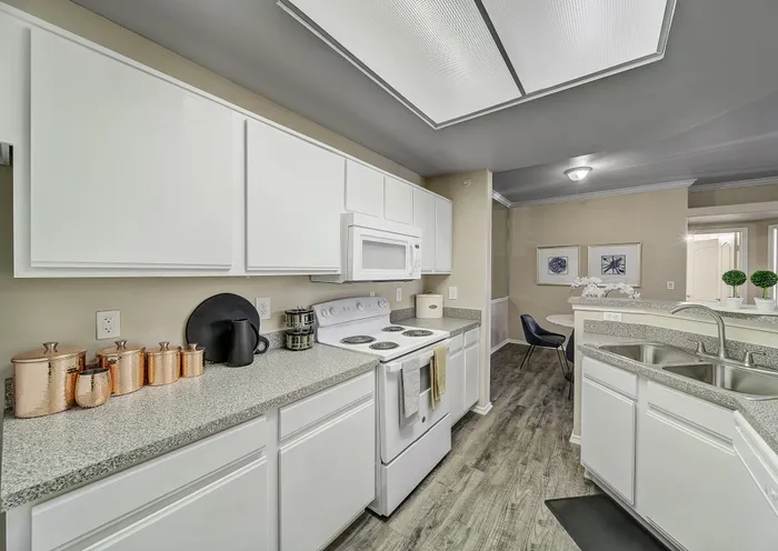 Modern kitchen with sleek white cabinetry, granite countertops, and stainless steel appliances, overlooking a cozy dining area. Bright and inviting space with elegant decor and wooden flooring.