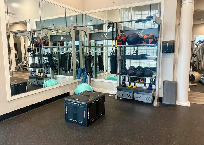 Modern fitness room with mirrored walls, featuring versatile gym equipment, stability balls, kettlebells, and boxing gear for a complete workout.