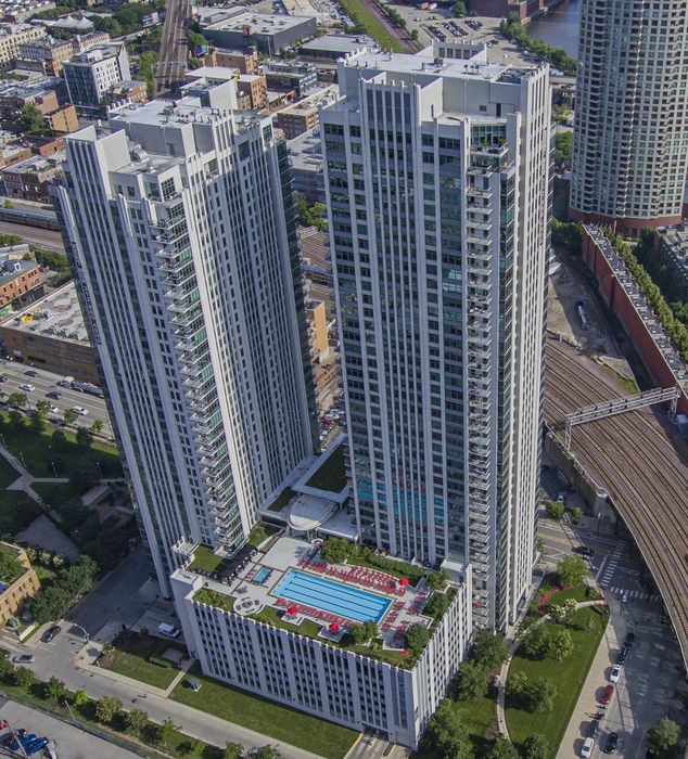 Elevated view of luxurious high-rise apartment complex featuring a rooftop pool, lush green spaces, and stunning cityscape vistas.