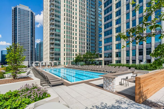 Luxurious urban apartment complex featuring a sparkling outdoor pool, elegant lounge chairs, and lush greenery surrounded by modern high-rise buildings.