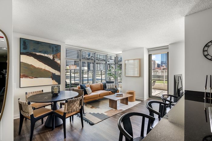 Bright and modern open-concept living space featuring a stylish seating area, dining table, and vibrant city views through expansive windows.