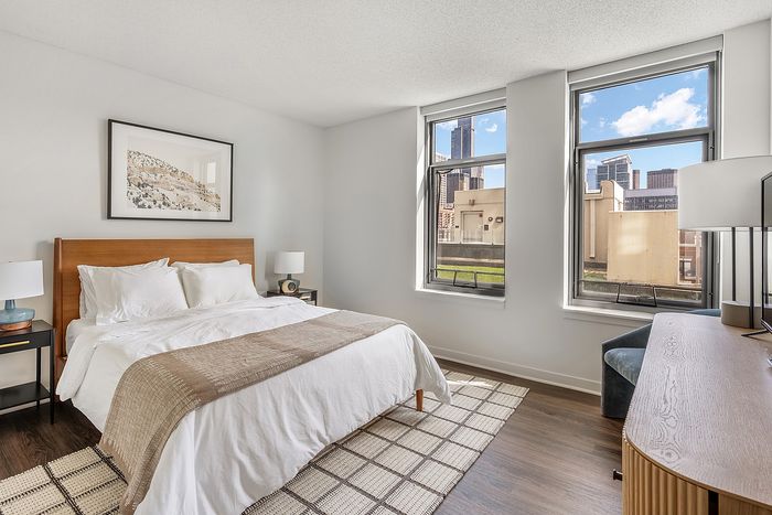 Bright, modern bedroom with elegant decor, cozy bed, and city views through large windows.