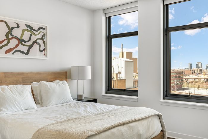 Bright and inviting bedroom with modern decor, large windows offering a stunning city view, and artistic wall art.