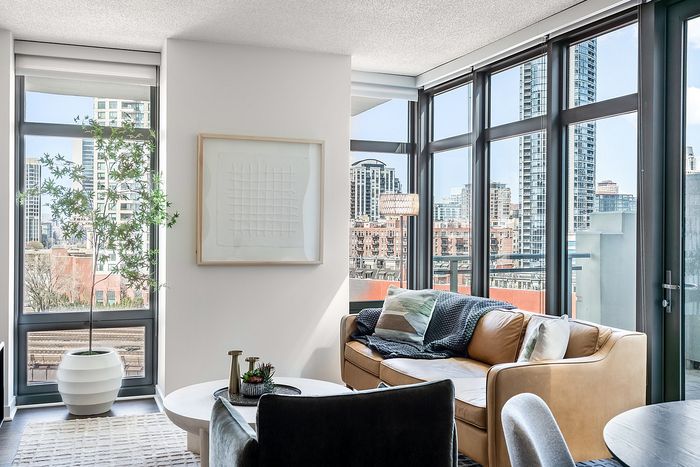 Bright and modern living room with floor-to-ceiling windows showcasing a stunning cityscape view, cozy seating, and stylish decor.